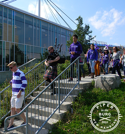 Bagpiper leading parade of students dressed in purple and white down stairs
