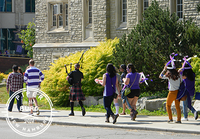 Bagpiper leading parade of students dressed in purple and white